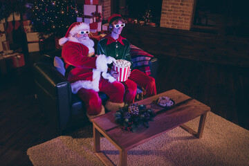 Photo portrait of santa claus taking popcorn from elf's lap watching movie on sofa in 3d glasses