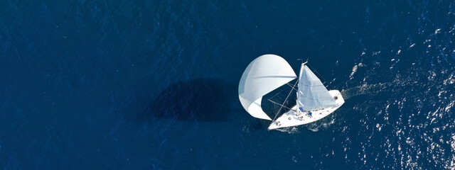 Aerial drone ultra wide panoramic photo of beautiful sailboat with white sails cruising deep blue...
