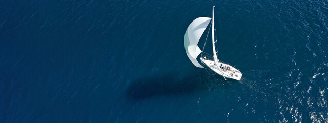 Aerial drone ultra wide panoramic photo of beautiful sailboat with white sails cruising deep blue...