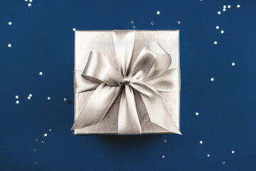 Silver gift box with bow on blue background. Flat lay, top view.