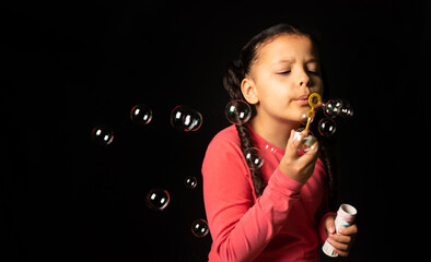 Brazilian girl with pink top playing soap bubbles, low key portrait, black background, selective focus.