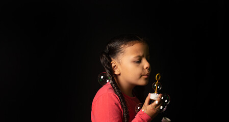 Brazilian girl with pink top playing soap bubbles, low key portrait, black background, selective focus.