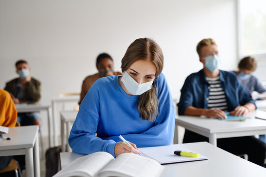 Young Students With Face Masks At Desks At College Or University, Coronavirus Concept.