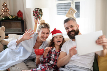 Family with small daughter indoors at home at Christmas, having video call.