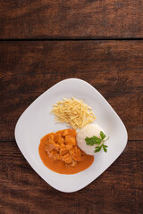 Rice, chicken stroganoff, potato straw in white dish, on wooden surface, gray background, top view.