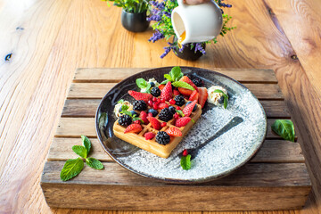 Belgian waffles with strawberries, blueberries, blackberries and syrup, homemade healthy breakfast, toned image, selective focus. Traditional belgian waffles with fresh fruit and whipped cream.