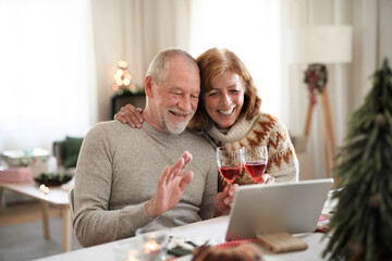 Senior couple indoors at home at Christmas, having video call with family.