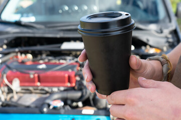 Holding a black paper cup on the background of a sports car