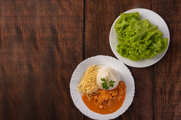 Rice, chicken stroganoff, potato straw and lettuce in white dish, on wooden surface, gray background, top view.