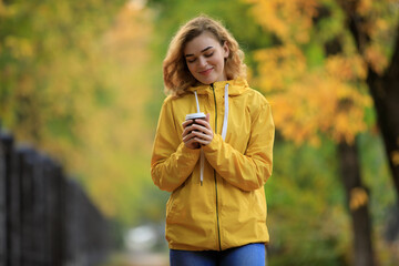 Fototapeta premium Woman in yellow jacket drinks a tea walking along fall alley