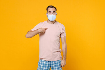 Shocked young man in pajamas home wear face mask safe from coronavirus virus covid-19 pointing index finger on himself resting at home isolated on bright yellow background. Relax good mood concept.