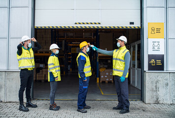 Group of workers with face mask in front of warehouse, coronavirus and temperature measuring...