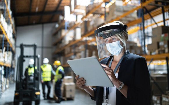 Manager with protective shield uisng tablet indoors in warehouse, coronavirus concept.