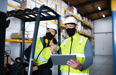 Workers with face mask and tablet working indoors in warehouse, coronavirus concept.