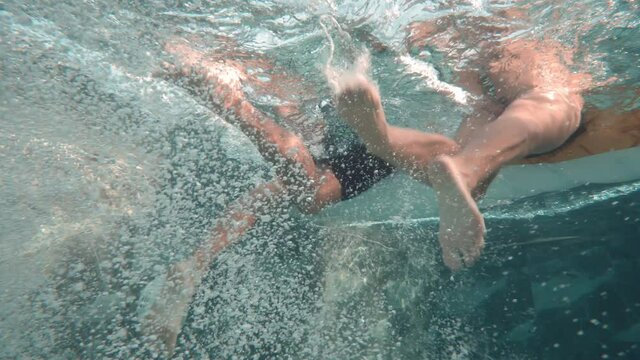 Underwater shot of female and male leg swings swimming underwater creating bubbles in blue pool hanging on waterbed