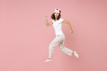 Full length side view portrait of cheerful young woman 20s in white pajamas home wear jumping like running while resting at home isolated on pastel pink background studio. Relax good mood concept.