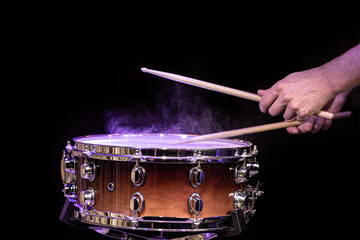 Drum sticks hitting snare drum with splashing water on black background under studio lighting.