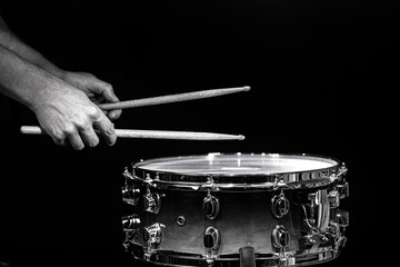 Drum sticks hitting snare drum with splashing water on black background under studio lighting....