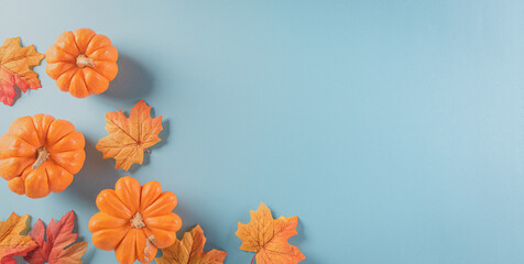 Thanksgiving background decoration from dry leaves and pumpkin on  pastel blue background. Flat lay, top view with copy space.
