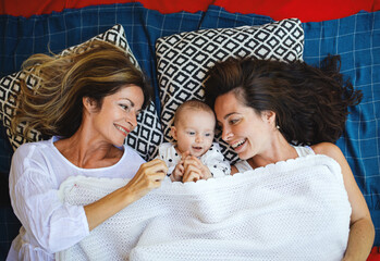 Top view of woman with daughter and baby granddaughter resting on blanket.