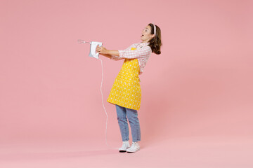 Full length portrait of shocked amazed young brunette woman housewife 20s wearing yellow apron hold mixer while doing housework isolated on pastel pink colour background studio. Housekeeping concept.