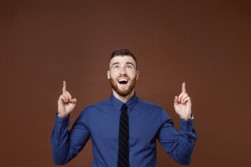 Surprised bearded young business man wearing blue shirt tie pointing index fingers up on mock up copy space isolated on brown background studio portrait. Achievement career wealth business concept.