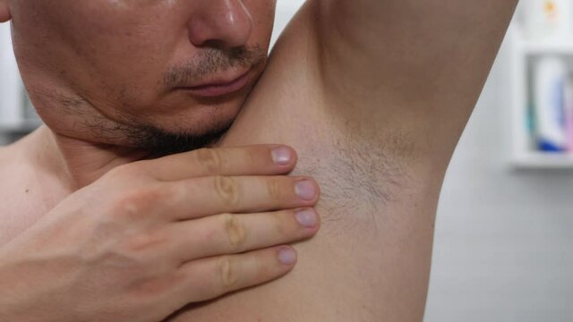 Natural underarm contains many sweat glands. Human left arm pit om white wall background. Touch axillary hair