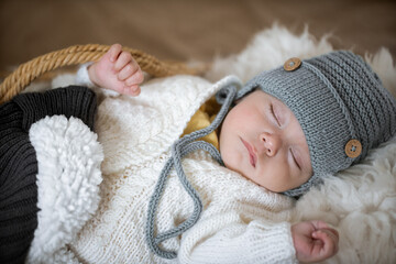 Portrait of a sleeping baby in a warm knitted hat with a knitted toy in the handle on a blurred background. Healthy sleep concept.
