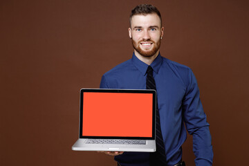 Smiling young business man in blue shirt hold laptop pc computer with blank empty screen mock up copy space isolated on brown background studio portrait. Achievement career wealth business concept.