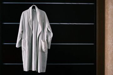 White robe in the hotel room. The hotel bathrobe weighs on a black cabinet