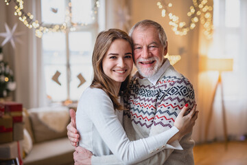 Senior man with young woman indoors at home at Christmas, hugging.