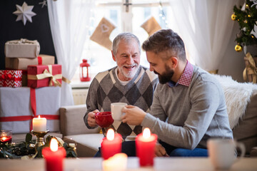 Mature man and senior father indoors at home at Christmas, drinking tea.