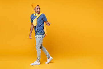 Fototapeta na wymiar Full length side view of smiling handsome young african american man 20s wearing blue t-shirt hat standing pointing index finger aside isolated on bright yellow colour background, studio portrait.