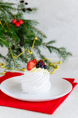 Pavlova cake on a red napkin against the background of a Christmas tree.