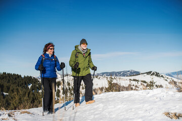 Senior couple with nordic walking poles hiking in snow-covered winter nature.