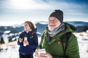 Senior couple hikers in snow-covered winter nature, drinking hot tea.