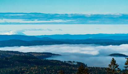 Fototapeta premium Morning fog in the valleys with a panoramic view over the boreal forest and snow covered mountains in the distance.