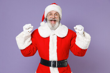 Fototapeta na wymiar Excited Santa Claus man in Christmas hat red suit coat white gloves glasses clenching fists doing winner gesture isolated on violet background studio. Happy New Year celebration merry holiday concept.