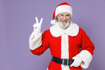 Fototapeta na wymiar Smiling gray-haired Santa Claus man in Christmas hat red suit coat white gloves glasses showing victory sign isolated on violet background studio. Happy New Year celebration merry holiday concept.
