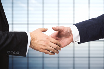 Handshake of two businessmen on the background of empty modern office, partnership concept, close up