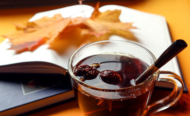 A Cup of hot tea with a spoon on the background of autumn leaves and books, close-up