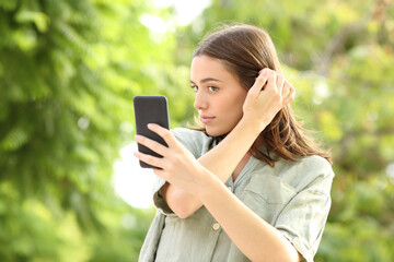 Woman combing using phone as a mirror in a park