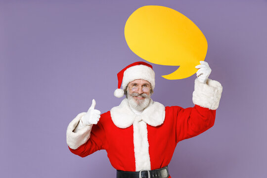 Funny Santa Claus man in Christmas hat red suit coat gloves glasses showing thumb up hold yellow empty blank Say cloud isolated on violet background. Happy New Year celebration merry holiday concept.