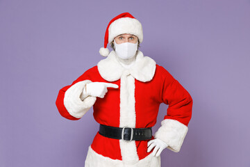 Fototapeta na wymiar Santa Claus man in Christmas hat red suit face mask to safe from coronavirus virus covid-19 pointing index finger on himself isolated on violet background. New Year celebration merry holiday concept.