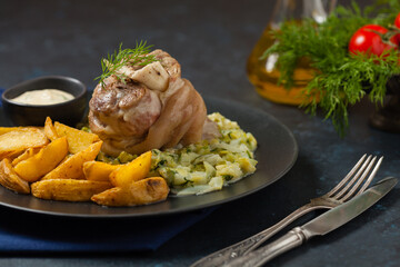 Boiled knuckle, served with cabbage and baked potatoes. Front view. Darkblue background. Dark mod.
