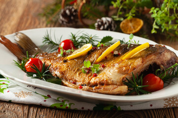 Fried carp whole. Served with lemon and cherry tomatoes on white plate. Christmas decoration.