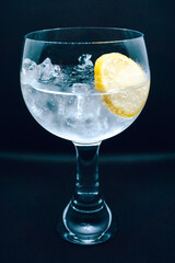 Gin and tonic cocktail with a lemon slice on black background. Alcohol, drink, ice, shallow depth of field, focus.