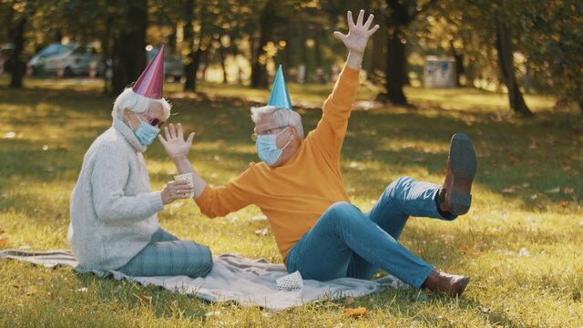 Anniversary celebration in the park during covid-19. Elderly couple with face mask having funny picnik in autumn. High quality photo