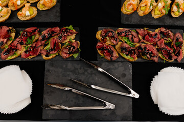 Bruschetta on black table with napkins and kitchen tongs