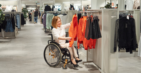 Woman shopper in a wheelchair chooses clothes in the mall. Christmas gifts, new year sale